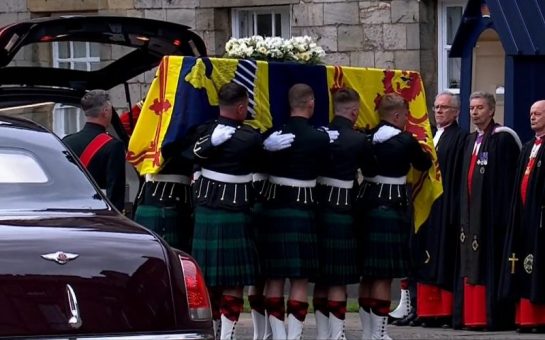 Queen Elizabeth's coffin wrapped in the Royal Standard of Scotland with a wreath of her favourite flowers from the Balmoral estate is carried into the Palace of Holyroodhouse's. Via iPlayer.