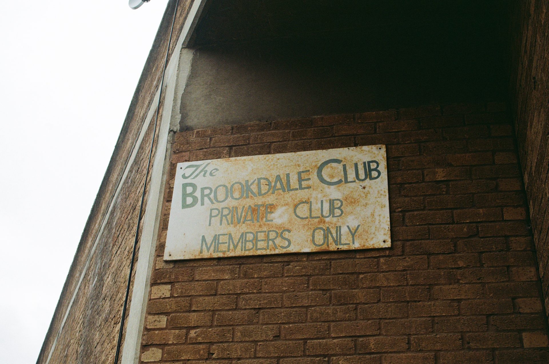 A sign which says 'the brookdale club private club members only' on a brick wall.