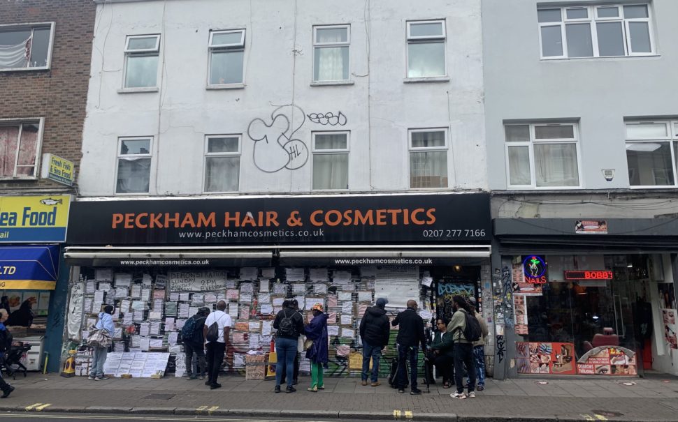 The image shows the shop front of Peckham Hair & Cosmetics, with campaigners gathering outside.