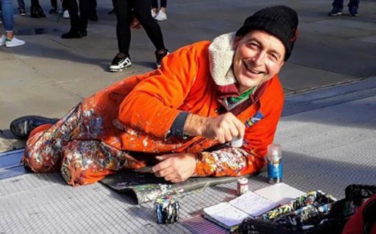 A photo of Ben Wilson in orange overalls painting a piece of chewing gum on the Millennium Bridge