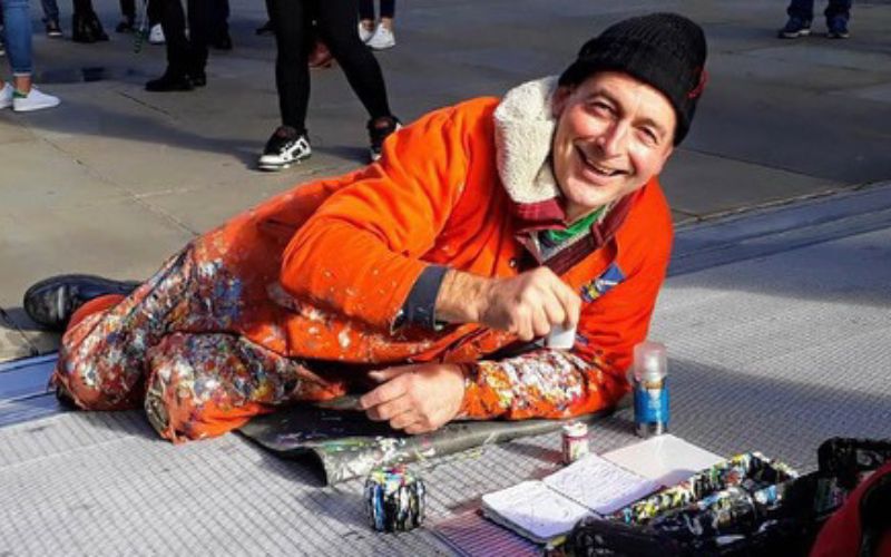 A photo of Ben Wilson in orange overalls painting a piece of chewing gum on the Millennium Bridge