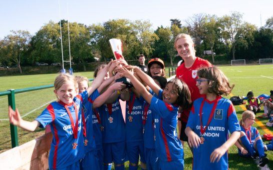 Young girls team lifting trophy with Chelsea player Aggie Beever-Jones