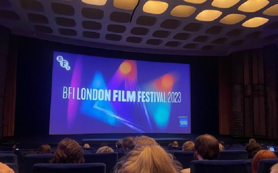 People sat in a cinema, they are looking at the screen that displays BFI London film festival 2023.