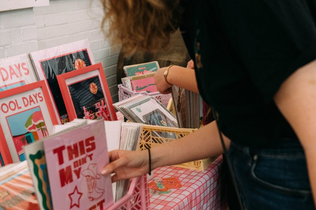 Shoppers browsing a bright and colourful stall selling art prints arranged on a gingham table cloth at a Salad Days market.