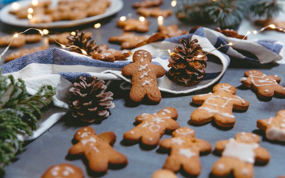 Many gingerbread men placed on a table along with some plates and pinecones