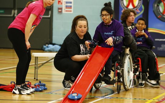 Disabled child using a slide to play an adapted version of curling.