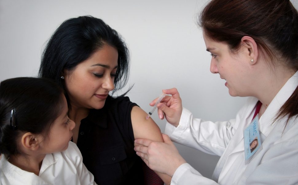 Woman receiving injection by female doctor with child on her lap