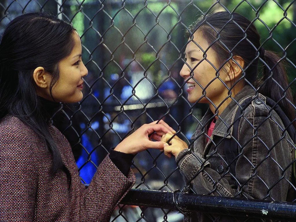 Two women hold hand with a fence in between