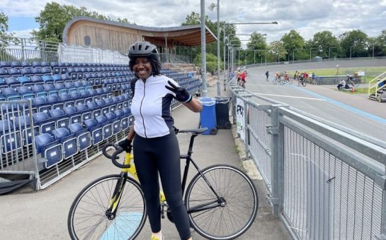 Bike Project recipient Aurore Longue stands proudly with her bike in her cycling lycra next to the track.