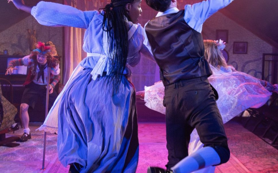 Two actors dancing with arms linked on a lit stage
