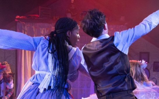 Two actors dancing with arms linked on a lit stage