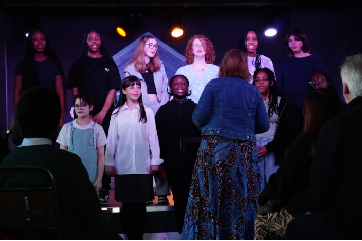 A group of children perform in front of a conductor