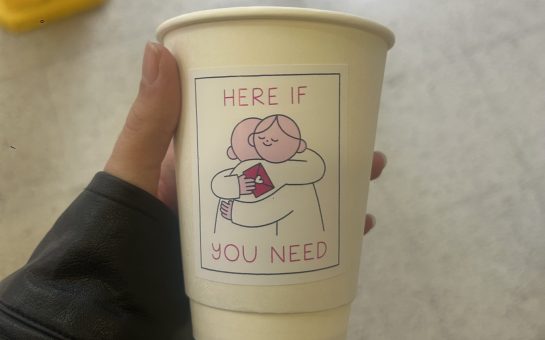 Someone holding a coffee cup with world mental health day artwork