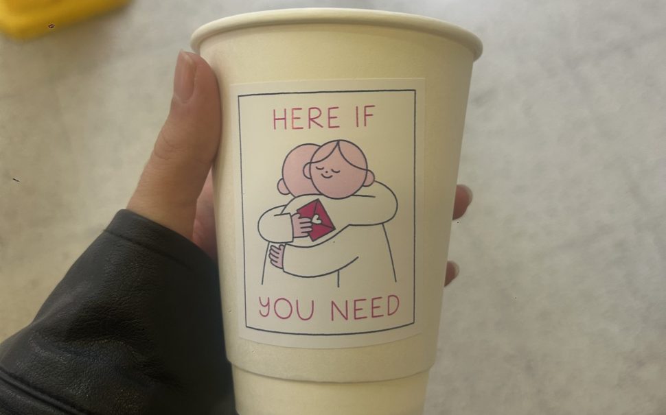 Someone holding a coffee cup with world mental health day artwork