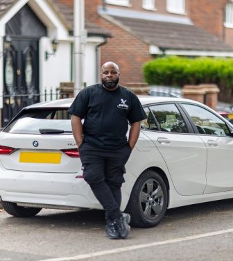 Man in all black posing in front of a white car