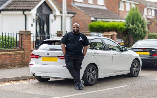 Man in all black posing in front of a white car