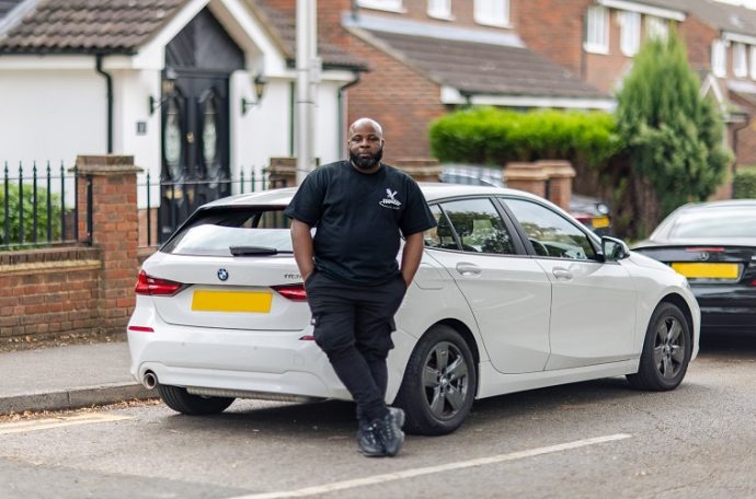 Man in all black posing in front of a white car