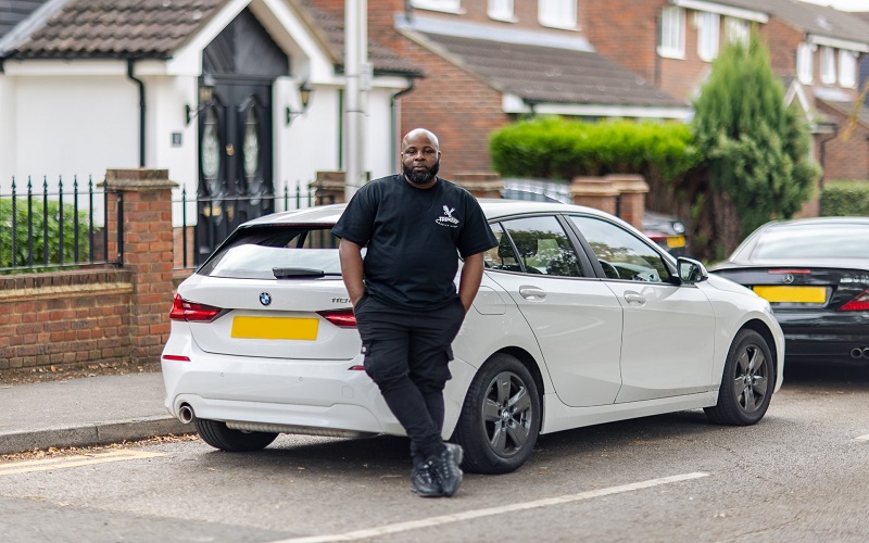 Man in all black posing in front of a white car