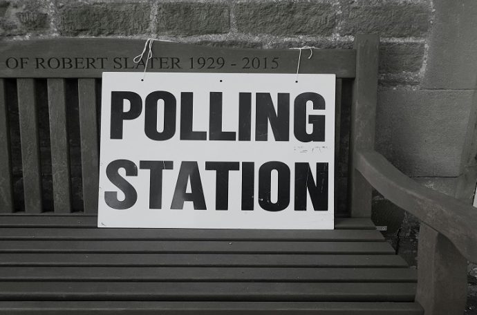 A picture of a sign saying "Polling Station" tied to a wooden bench. Photo by Steve Houghton-Burnett on Unsplash