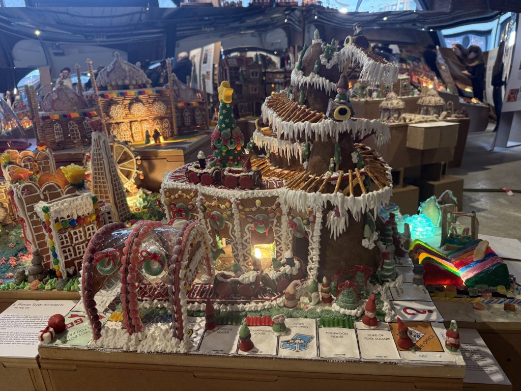 A gingerbread Monopoly board featuring a chessboard of friendly competition, and a mountain filled with elves, Christmas trees and Santa's hidden workshop. A playful rollercoaster links everything.