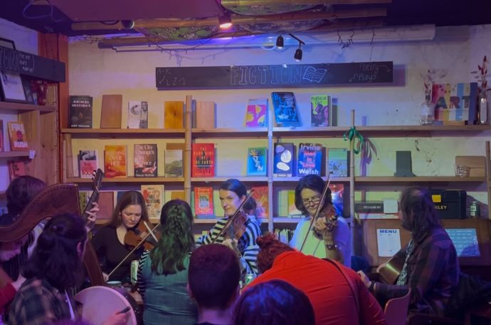 Photo: the bookshop, with the folk music night in full swing. Customers enjoying themselves in the foreground, musicians playing violins in the background