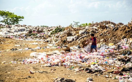 Boy walking through piles of rubbish holding cardboard box