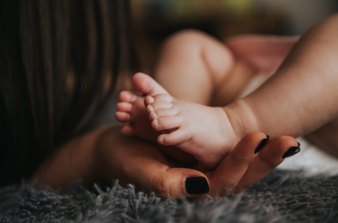 A child's foot being held by a mother's hand.