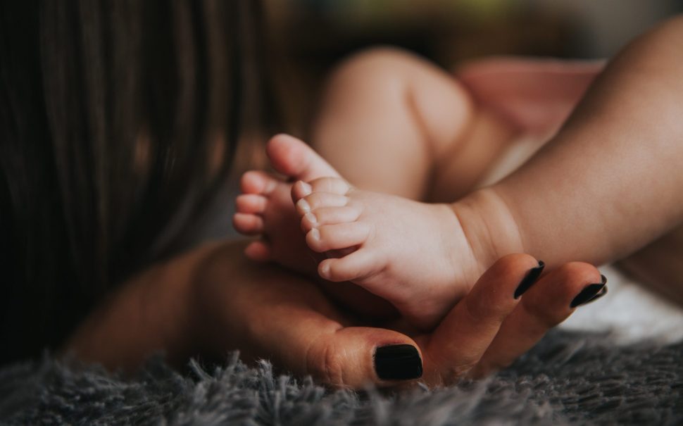 A child's foot being held by a mother's hand.