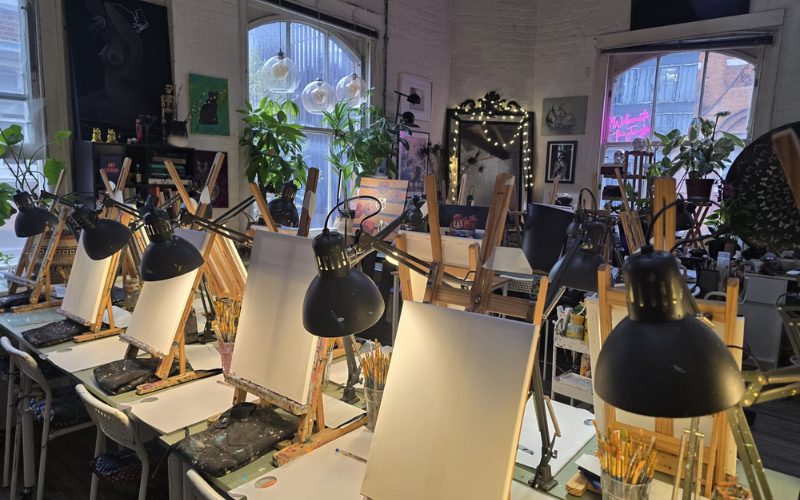 A photo of the Art Social Club studio. There is a table with easels and canvases dimly lit.
