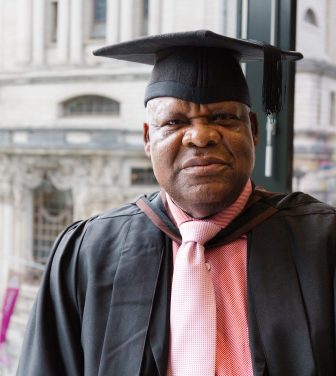 Chris Osagbaekhoe stands by a window in academic dress for his graduation