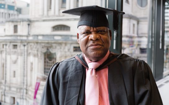 Chris Osagbaekhoe stands by a window in academic dress for his graduation