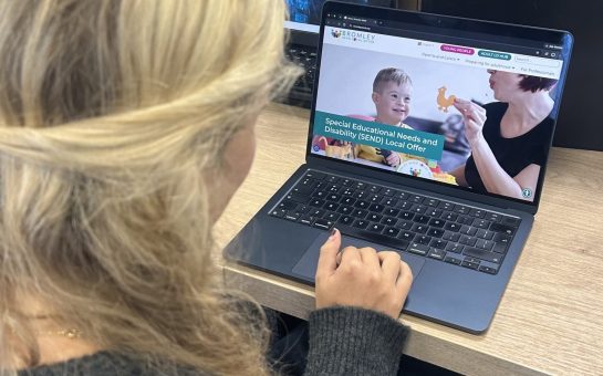 A young person in a black cardigan is on a laptop, which is open on the Bromley SEND Local Offer website.
