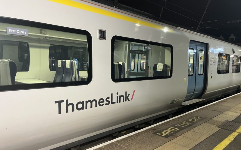 Photograph of a Thameslink Class 700 train, taken at night. The side of a white train carriage and blue sliding doors are visible.
