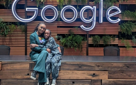Keighley Douglas and her daughter Raiyah sitting together beneath a large illuminated Google sign.