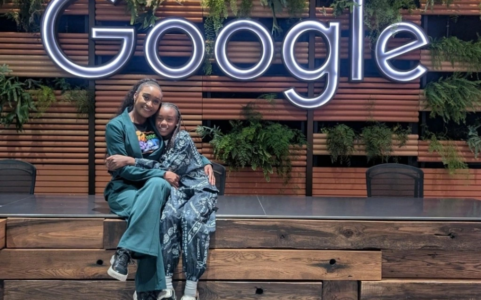 Keighley Douglas and her daughter Raiyah sitting together beneath a large illuminated Google sign.